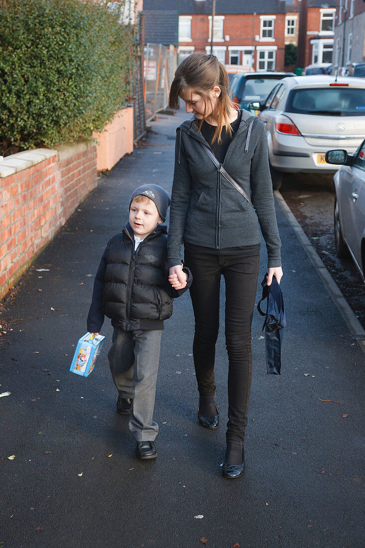 Teenage sister walking young brother to primary school