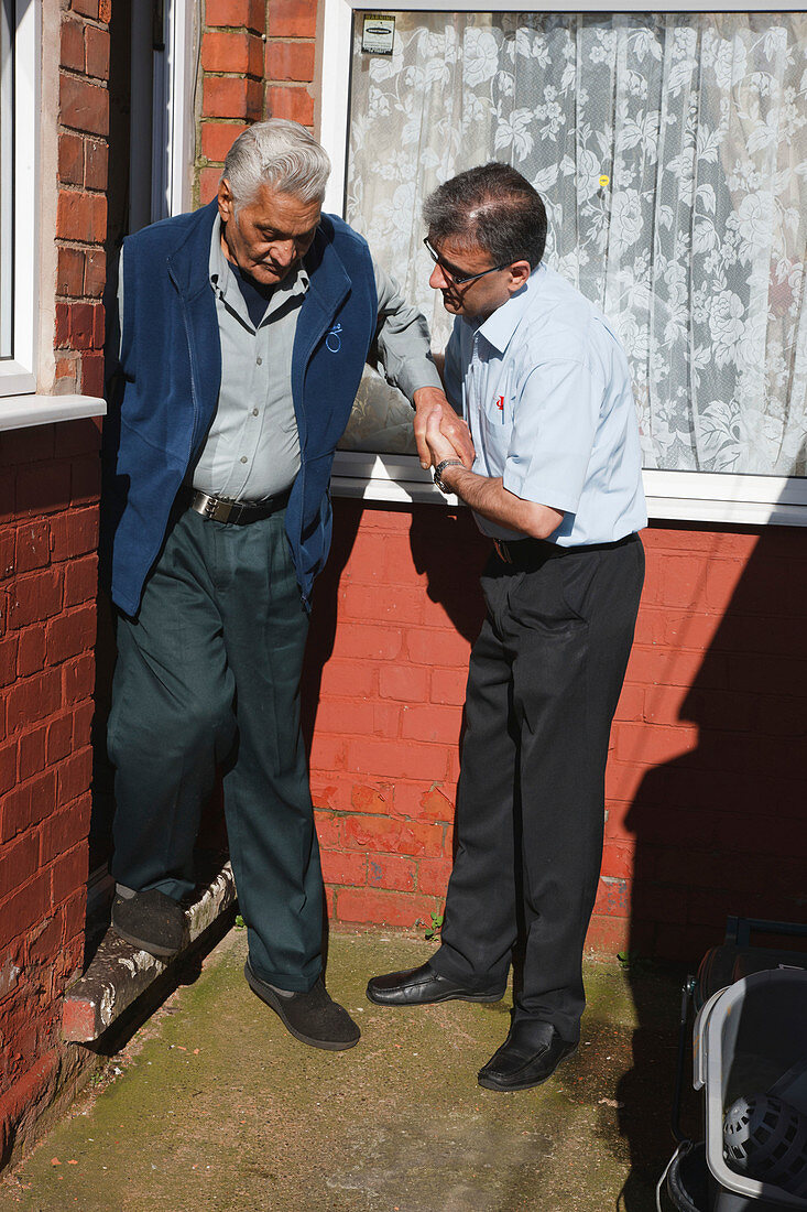 Son helping elderly south Asian father down step