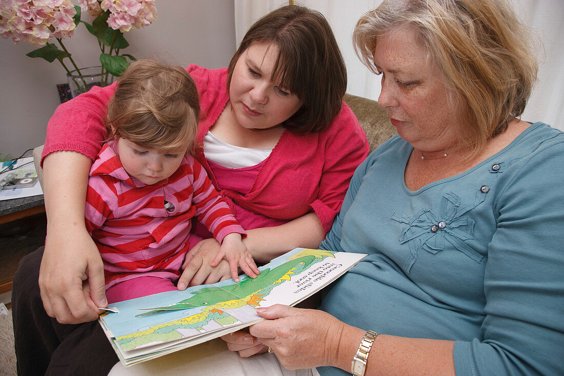 Toddler with her mum and grandmother reading a book