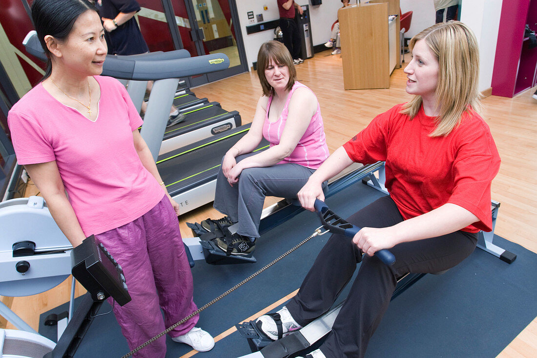 Fitness instructor showing women how to use a rowing machine