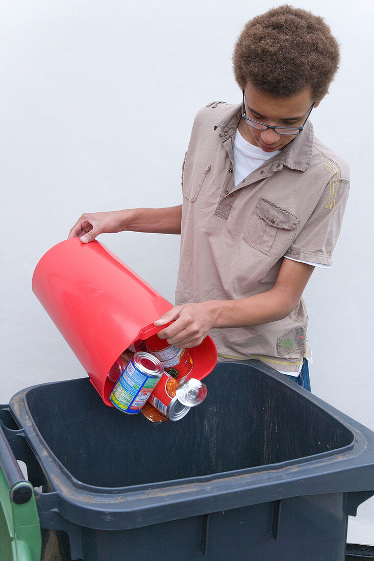Teenage boy putting tins and cans into recycling wheelie bin