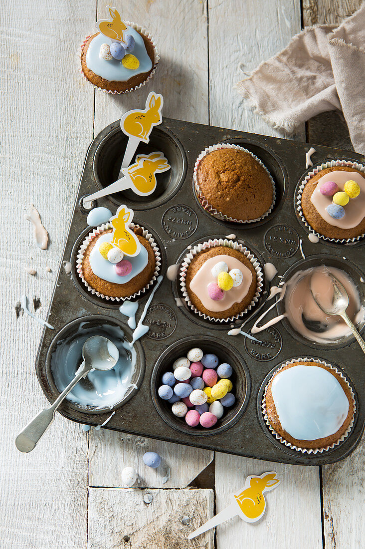 Vintage baking tray filled with cupcakes being decorated with Easter themed decorations