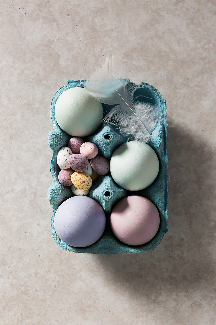 Easter Dyed Eggs in a box with chcolate mini eggs, overhead with a white feather