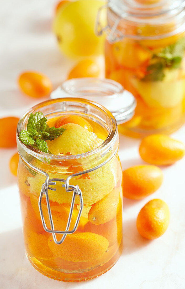 Selbstgemachter Kumquat-Essig im Glas mit ganzen Früchten, Zitronenschale und frischer Minze