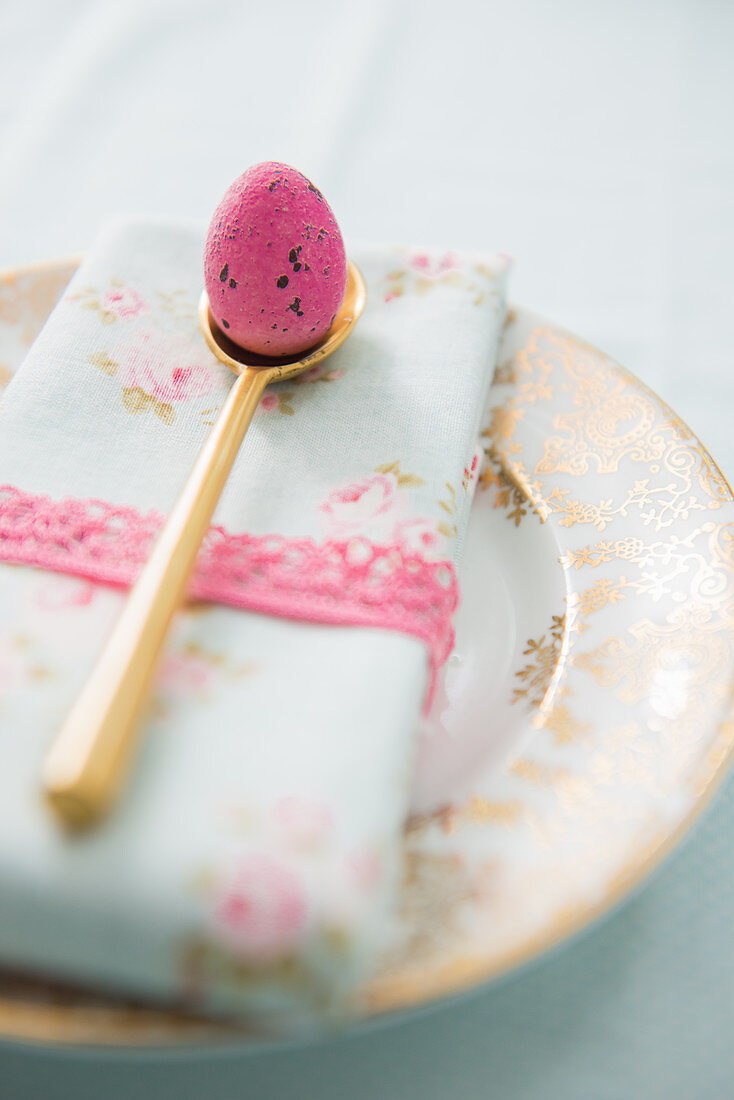 Rosafarbenes Ei auf goldenem Löffel und Serviette auf einem Teller