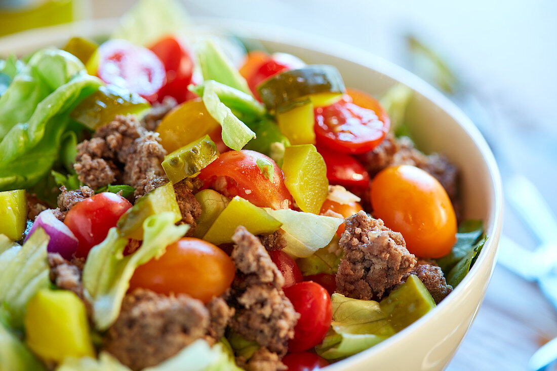 A hamburger salad with minced meat, lettuce, tomatoes, gherkins and cheese