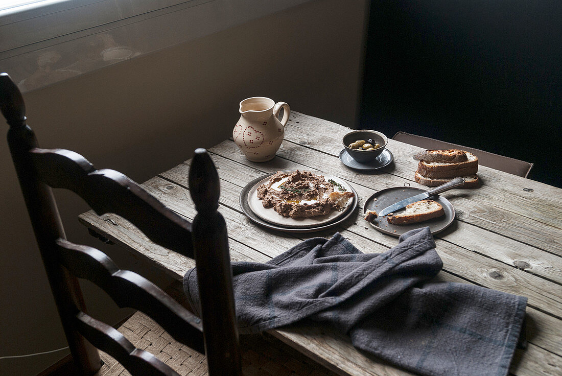 Linsen-Shiitakecreme mit Brot und Oliven auf rustikalem Holztisch
