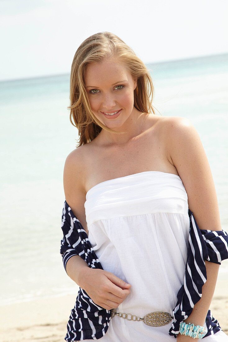 Junge Frau in weißem Sommerkleid und gestreiftem Jäckchen am Strand