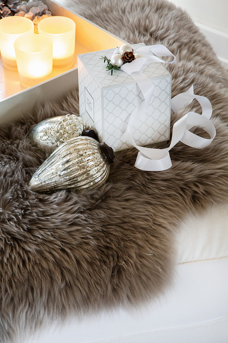 Christmas-tree bauble, gift box and tray of tealights on fur rug