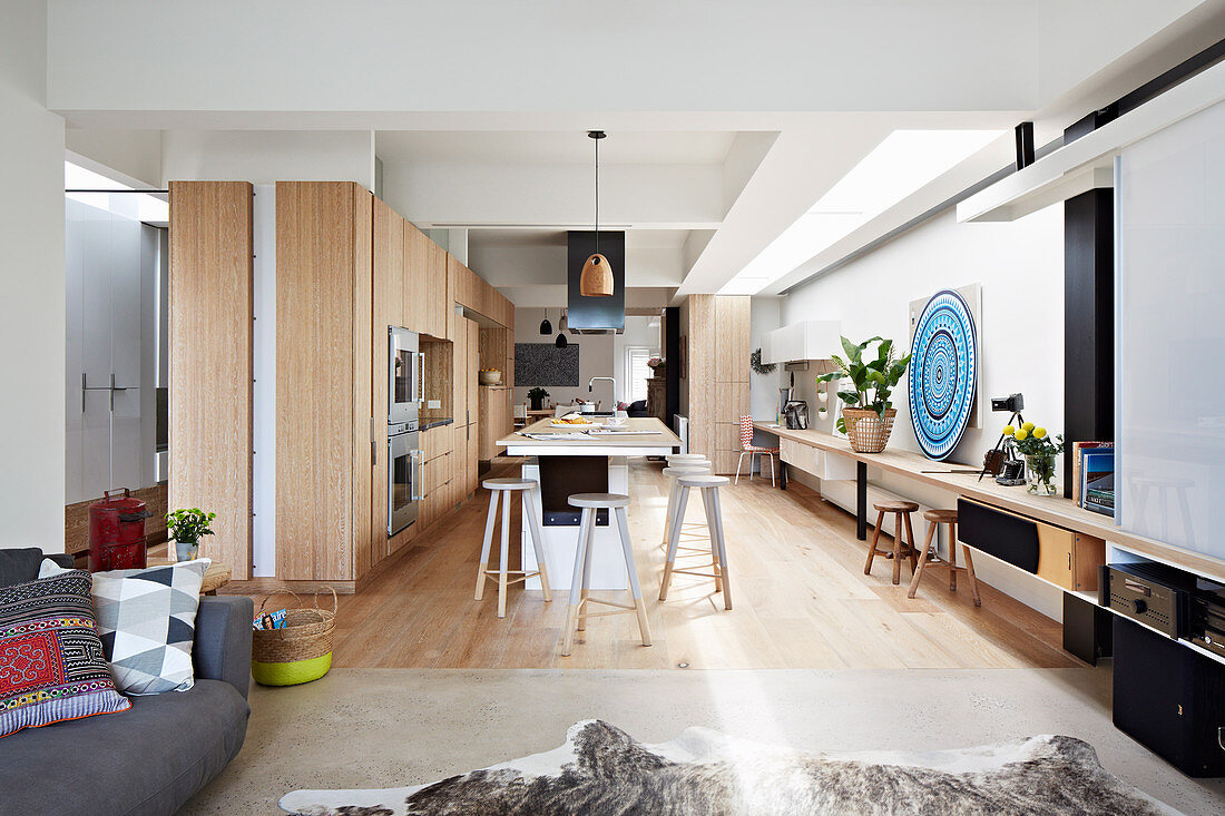 Einbauküche mit Holzfronten und Kochinsel, durchgehende Holzplatte als Schreibtisch in offenem Wohnraum