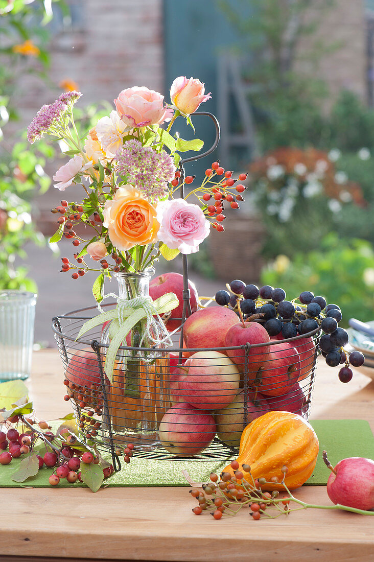 Thanksgiving with bouquet of roses, rose hips and stonecrop in basket with apples