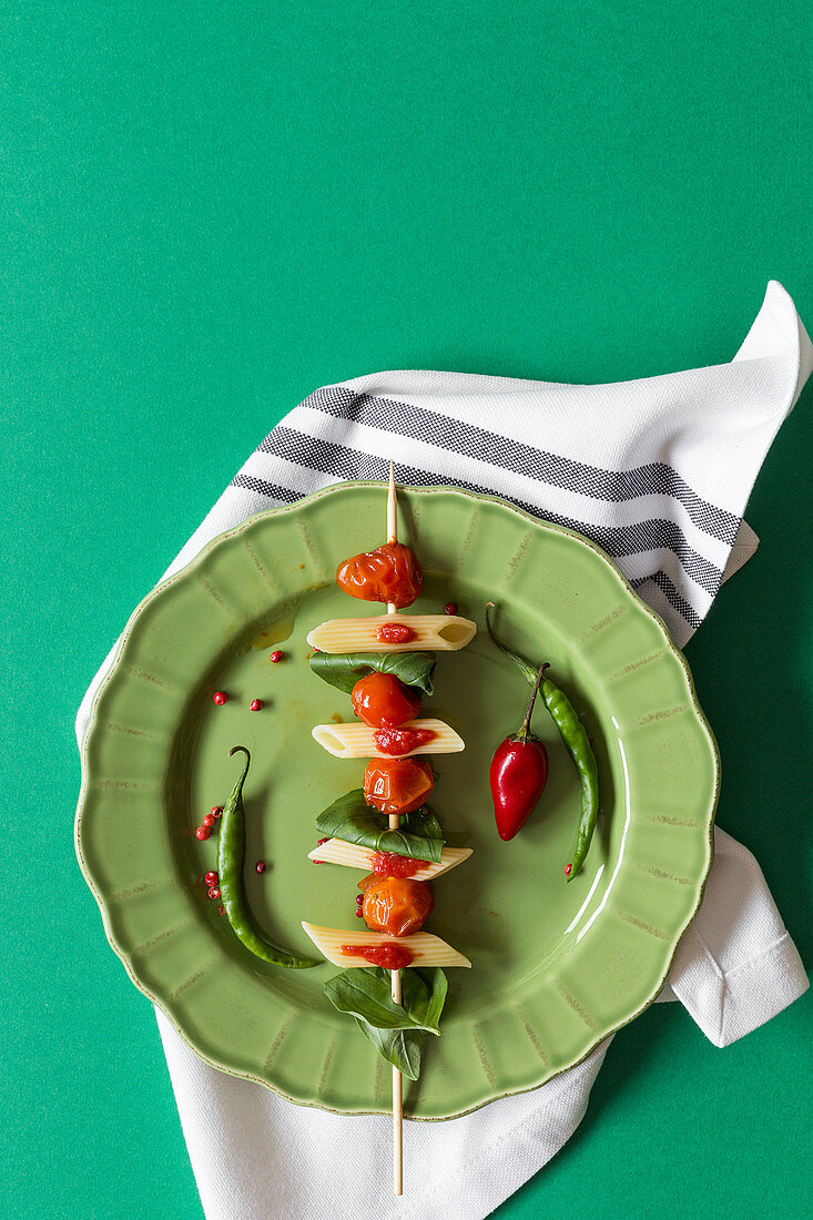 Nudelspieß mit Penne, Tomaten und Basilikum auf grünem Teller