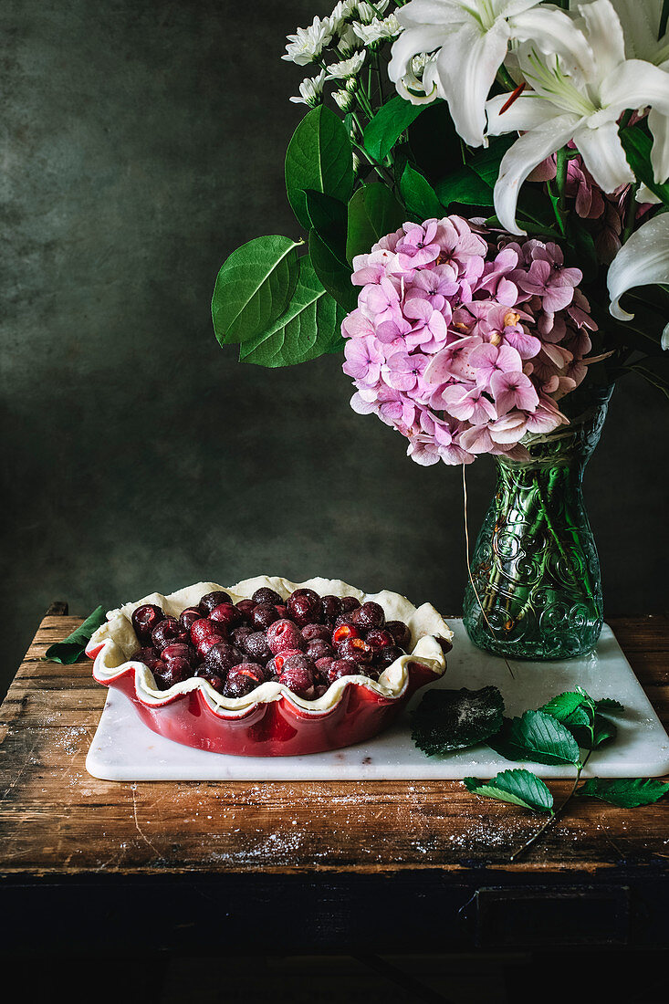 Flat lay of baked cherry pie with lattice top crust served on rustic table with green leaves around