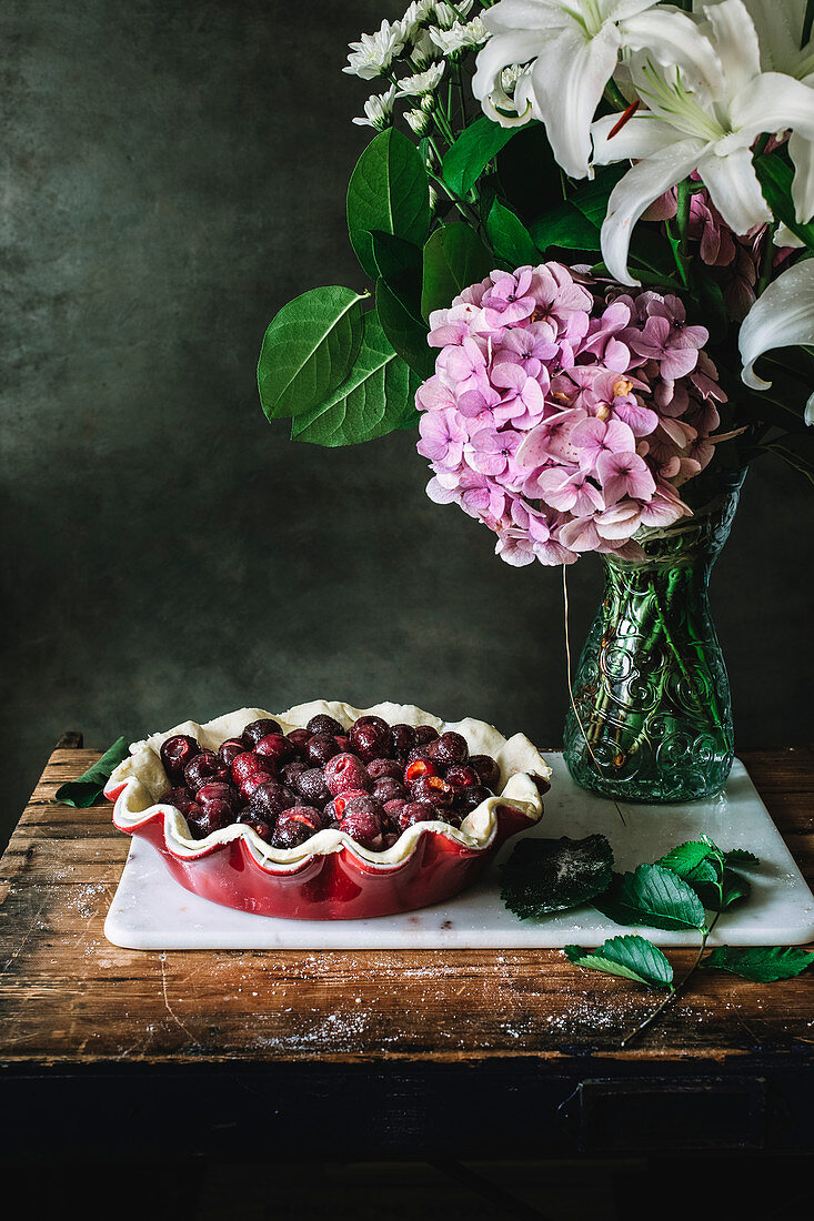 Ungebackener Kirschkuchen und Blumenstrauss auf rustikalem Holztisch