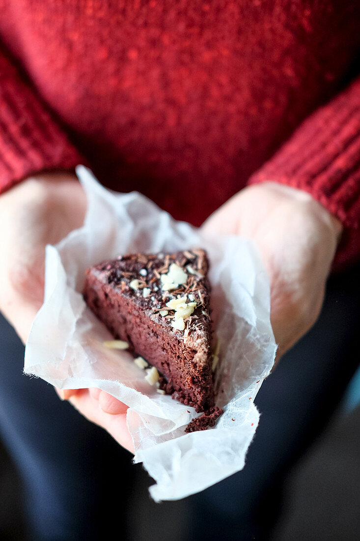 Hände halten ein Stück Rote-Bete-Kuchen mit gehackten Nüssen und Schokolade
