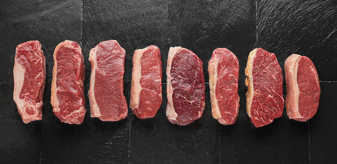 Verschiedene rohe Steaks auf einer schwarzen Schieferplatte