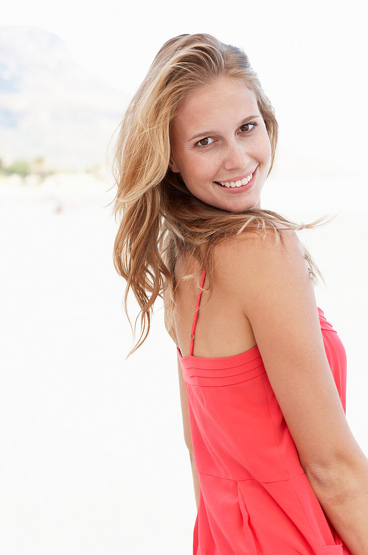 Junge blonde Frau in rotem Sommerkleid am Strand