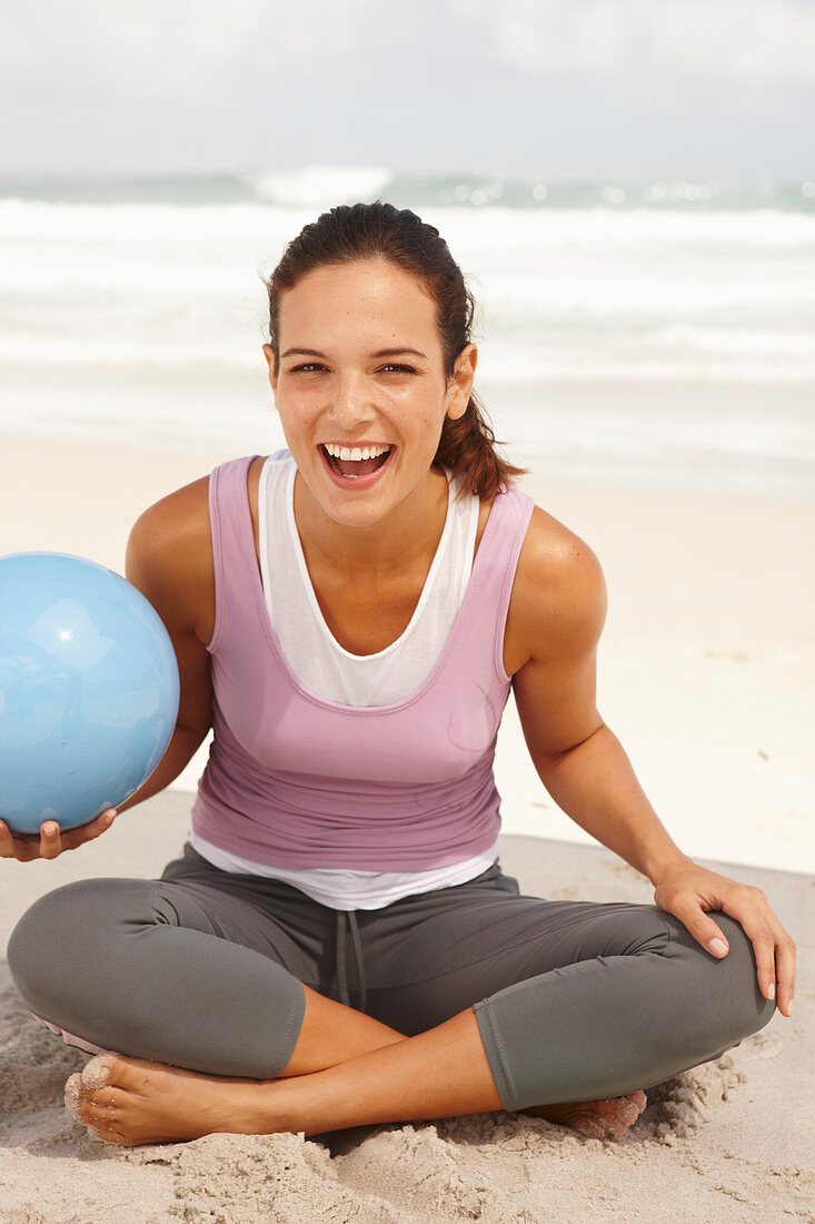 Junge brünette Frau mit Ball im Lotussitz am Meer