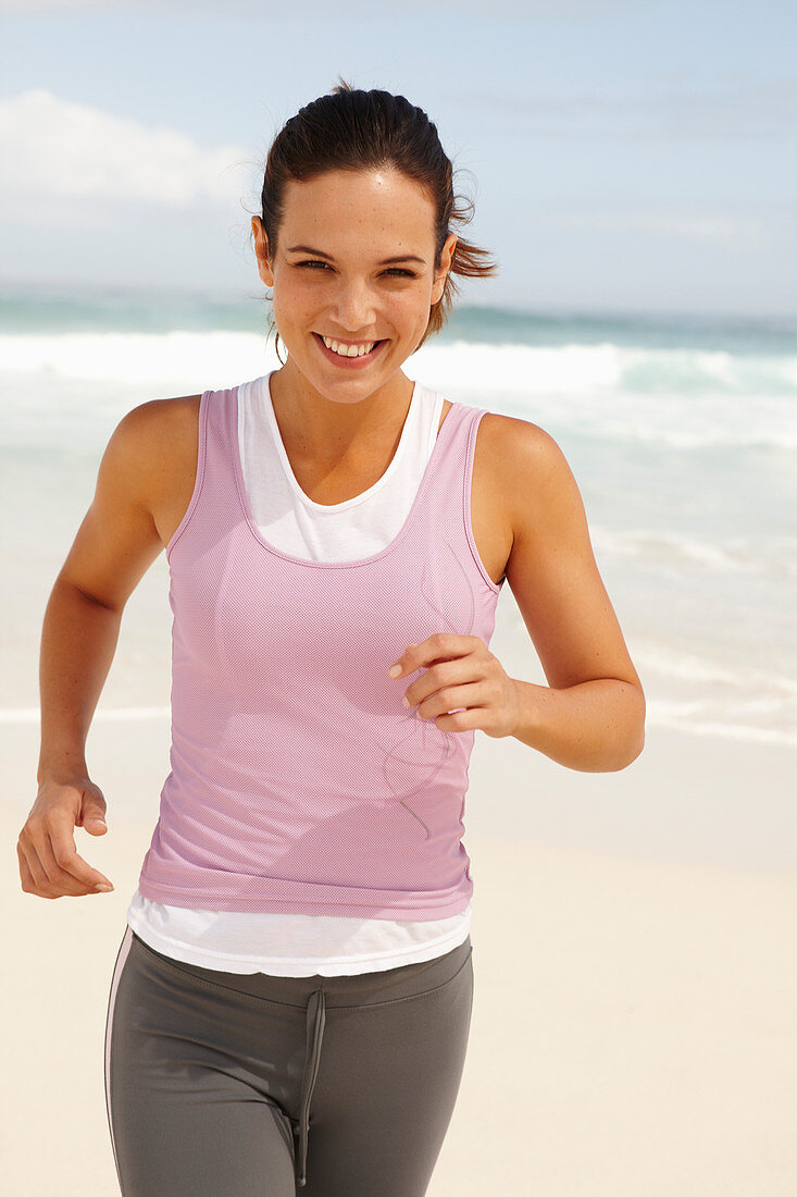 Junge brünette Frau in sportlicher Kleidung joggt am Meer