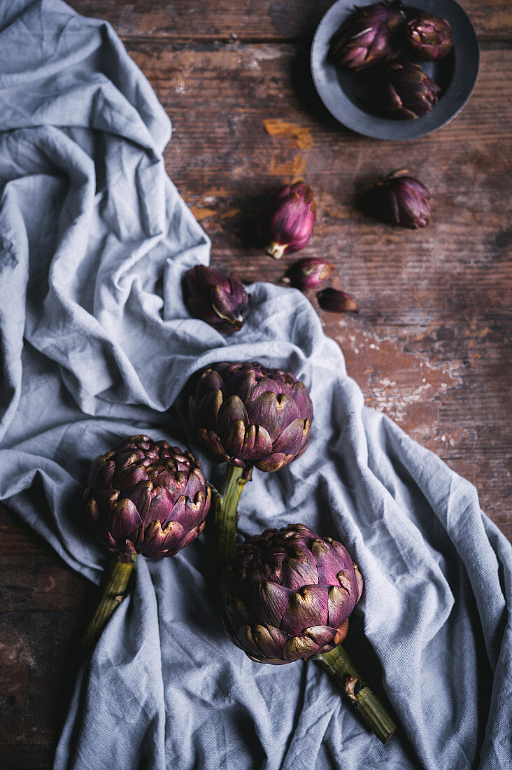 Large and small violet artichokes on a cloth and a wooden surface
