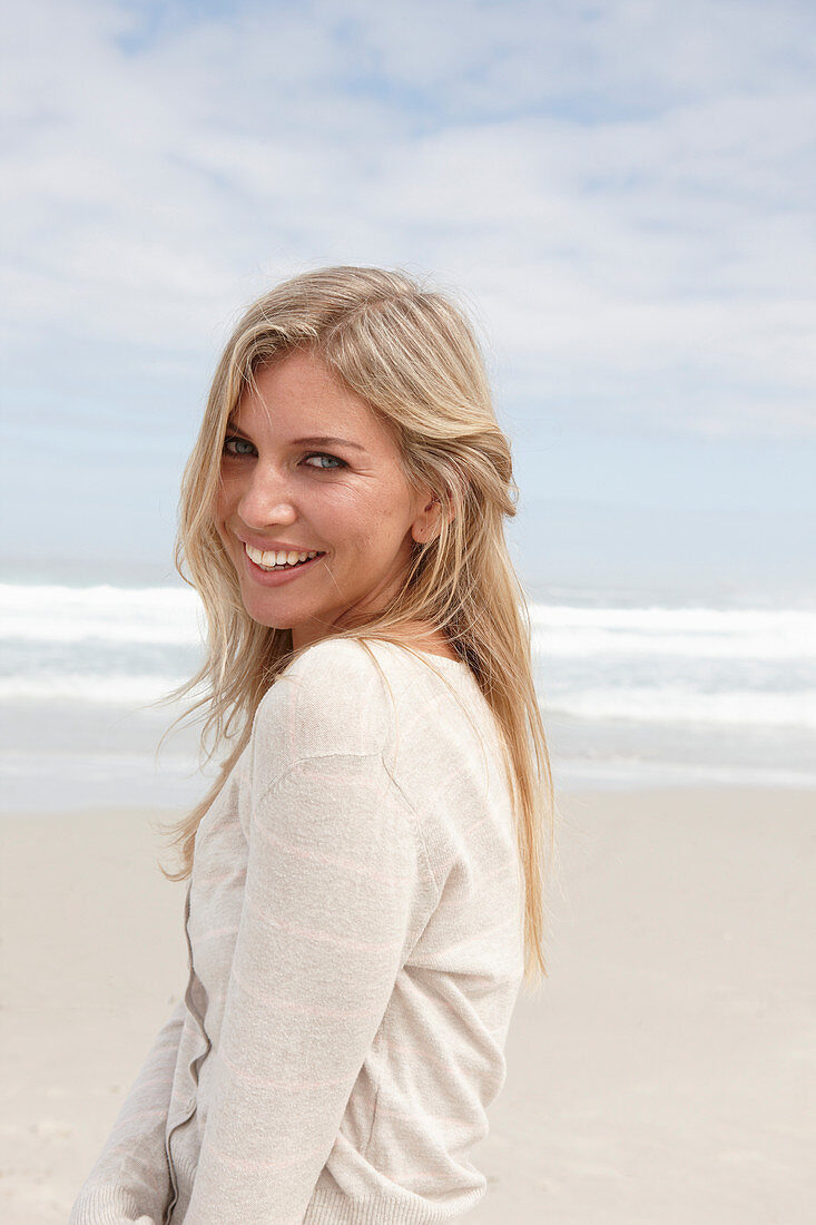 Blonde Frau in hellem Cardigan am Strand