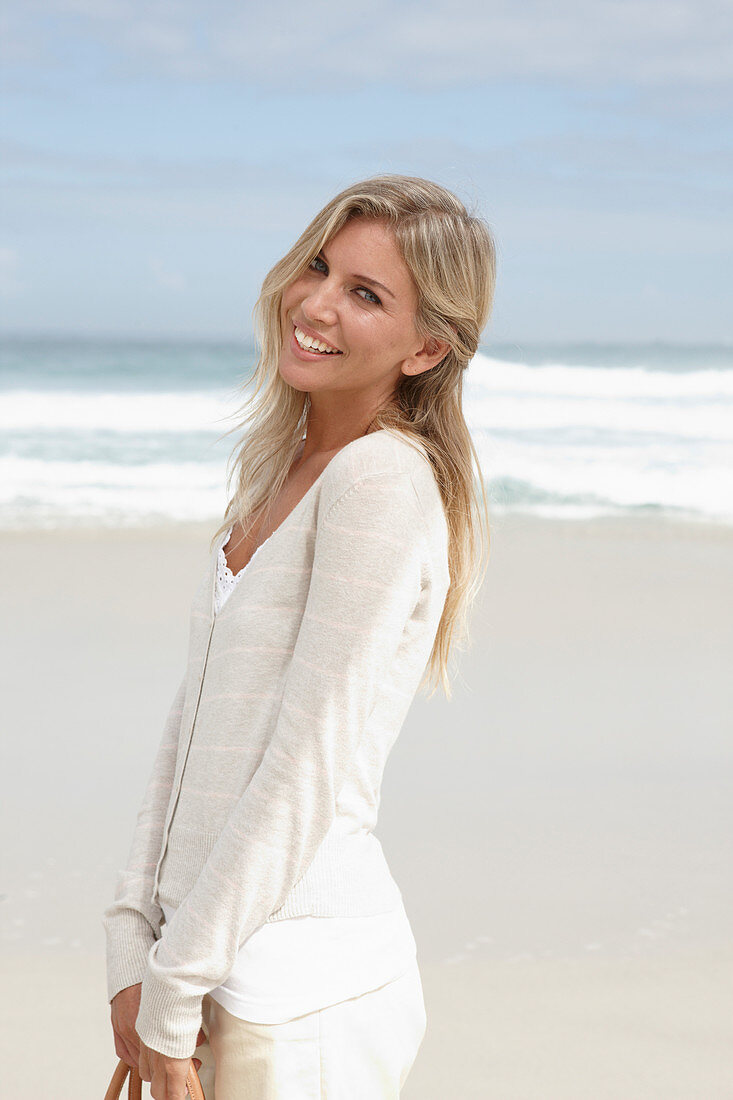 Blonde Frau in hellem Cardigan und Shorts am Strand