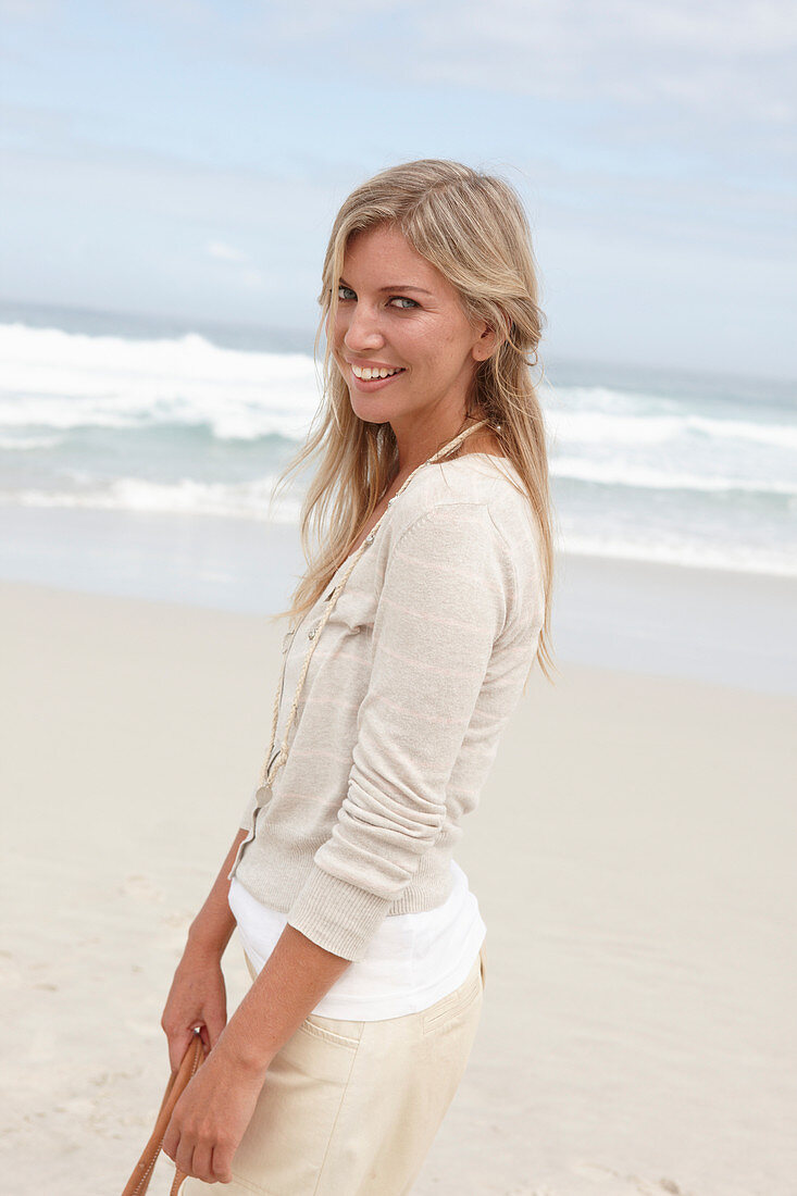 Blonde Frau in hellem Cardigan und Shorts am Strand