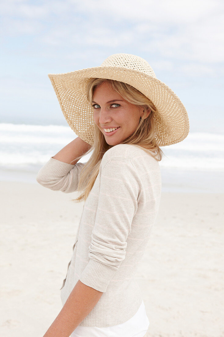 Blonde Frau mit Sommerhut in hellem Cardigan am Strand