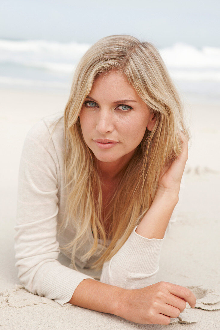 A blond woman on a beach wearing a light cardigan