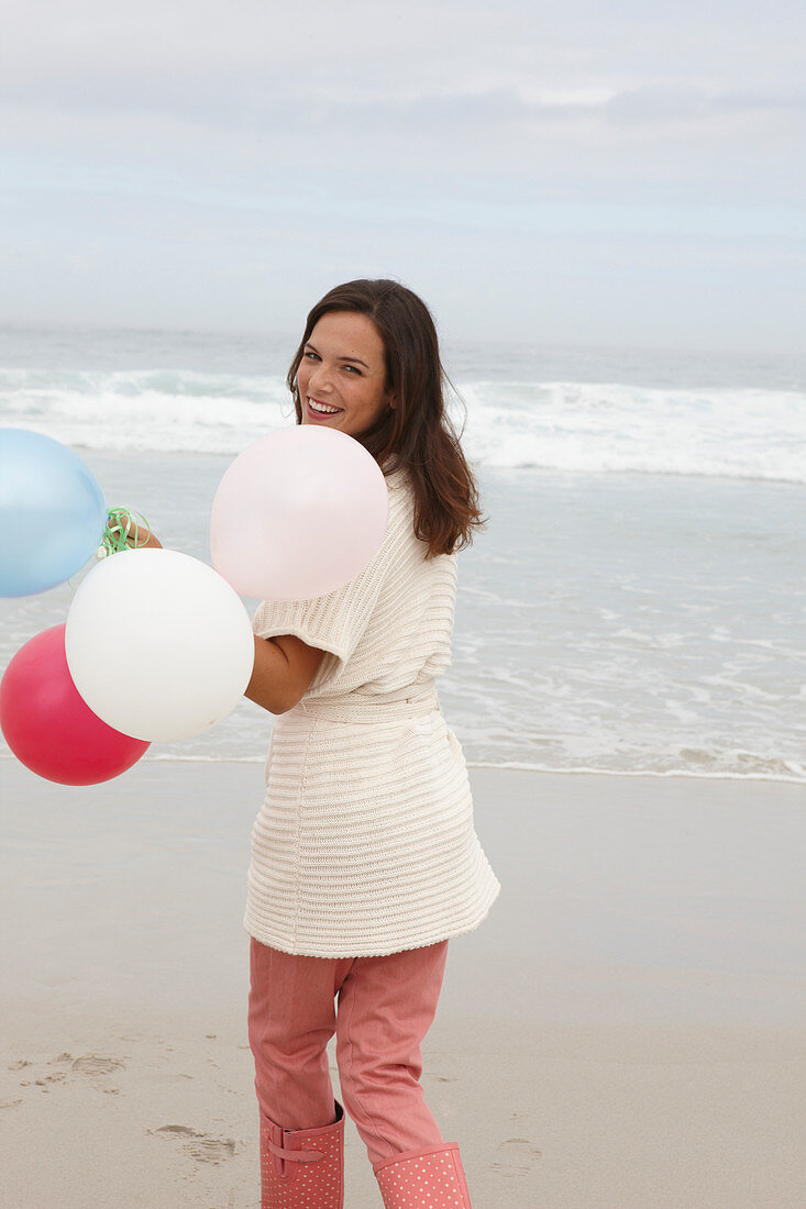 A brunette woman wearing a short-sleeved cardigan and holding a balloon