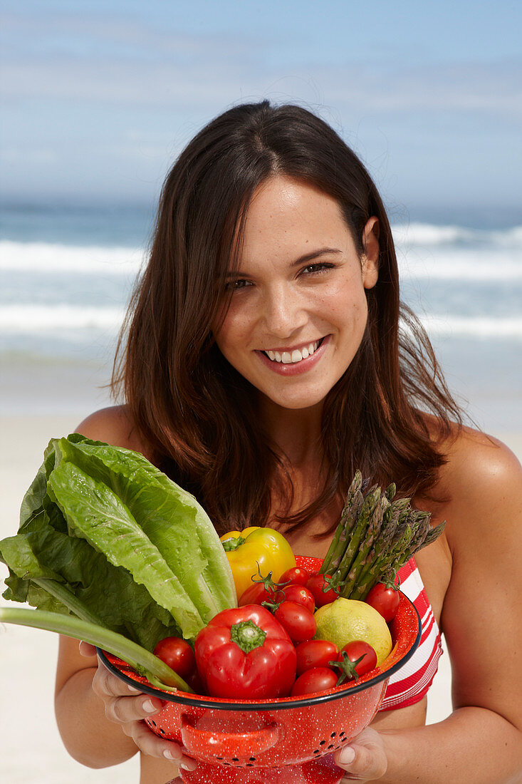 A young brunette woman on a beach holding a bowl of vegetables