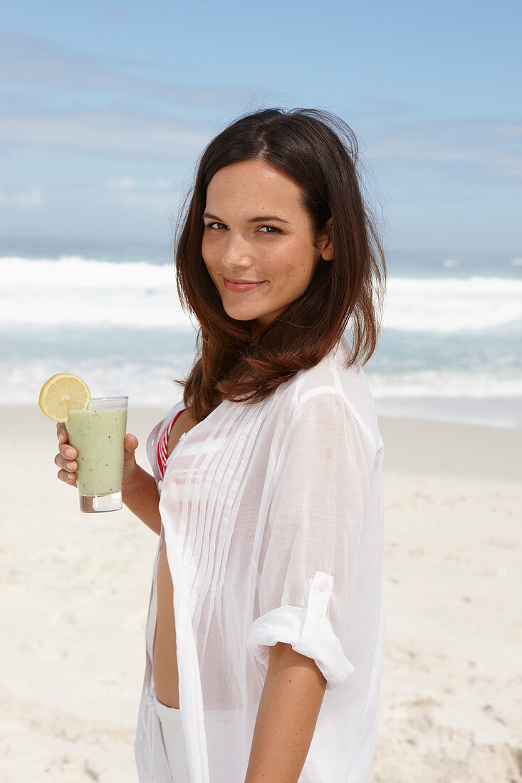 A young brunette woman on a beach with a smoothie wearing a white shirt