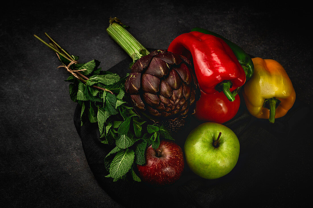 Paprika, Artischocke, Minze und Äpfel auf dunklem Untergrund