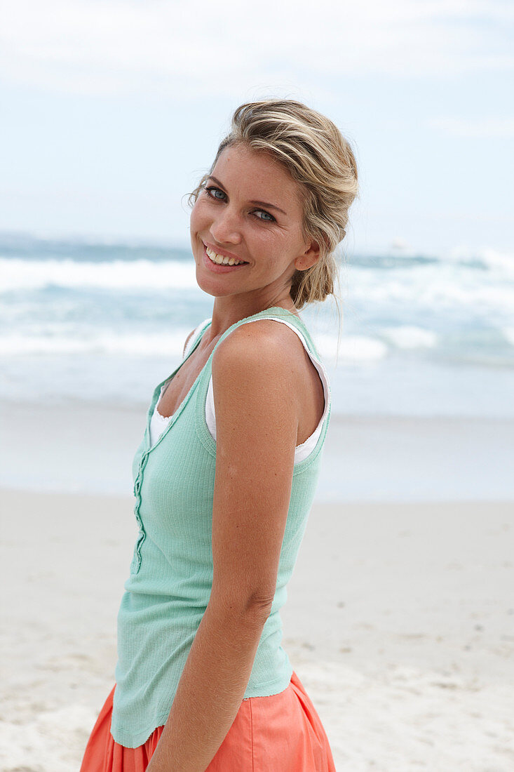 A blonde woman on a beach wearing a turquoise top