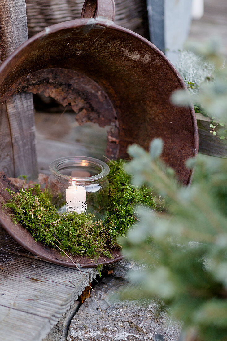 Candle in mason jar and moss arranged in metal bucket with rusted-through bottom