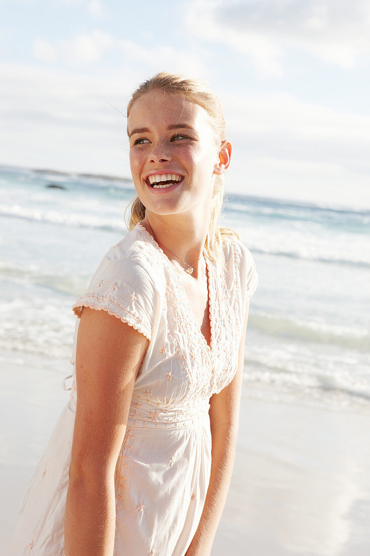 A blonde woman by the sea wearing a white embroidered dress