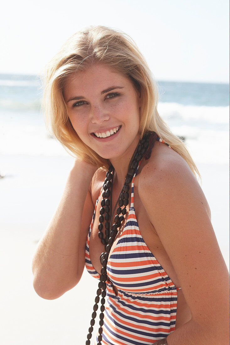 Junge blonde Frau in gestreiftem Badeanzug am Strand