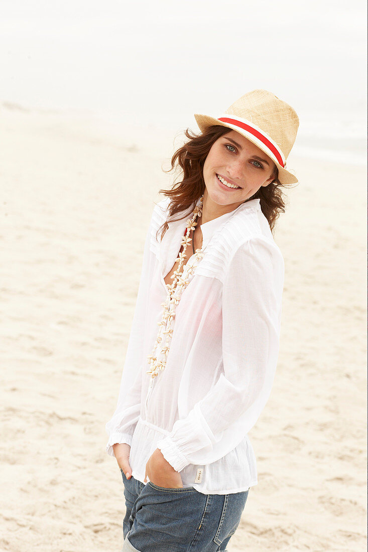 A brunette woman wearing a hat, a white blouse and denim shorts