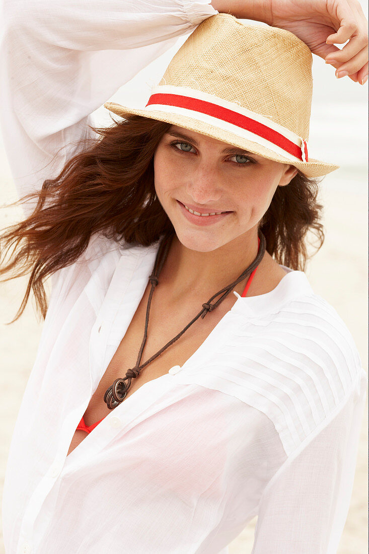 A brunette woman wearing a hat, a red bikini top and a white blouse