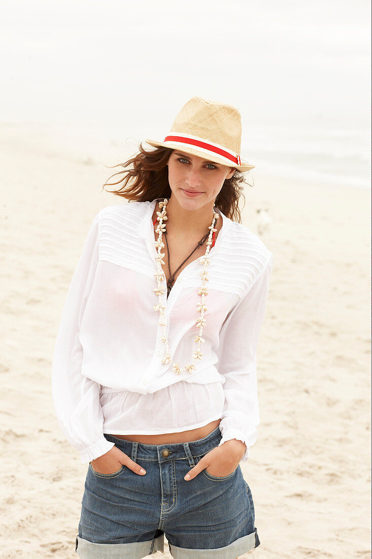 A brunette woman wearing a hat, a white blouse and denim shorts