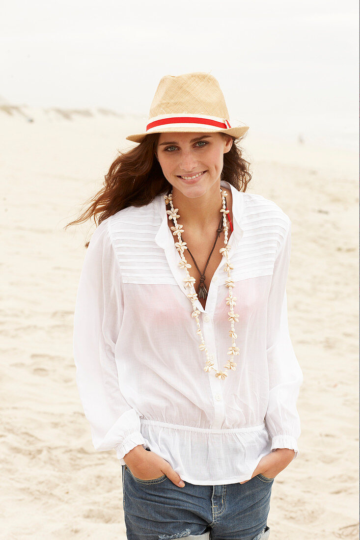 A brunette woman wearing a hat, a white blouse and denim shorts