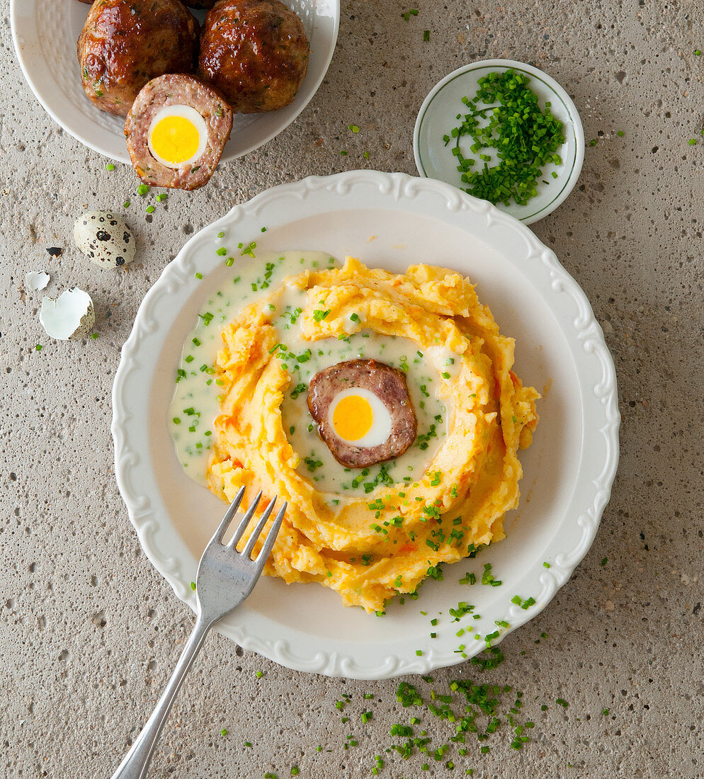 A meatball with a quail's egg on a bed of mashed potatoes and carrots with chive sauce