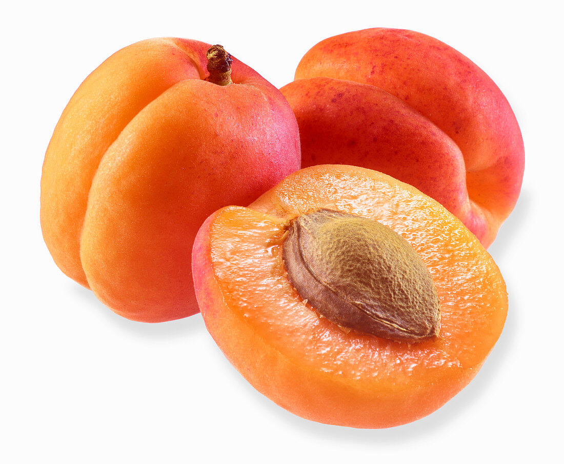 Two apricots and half an apricot on a white surface
