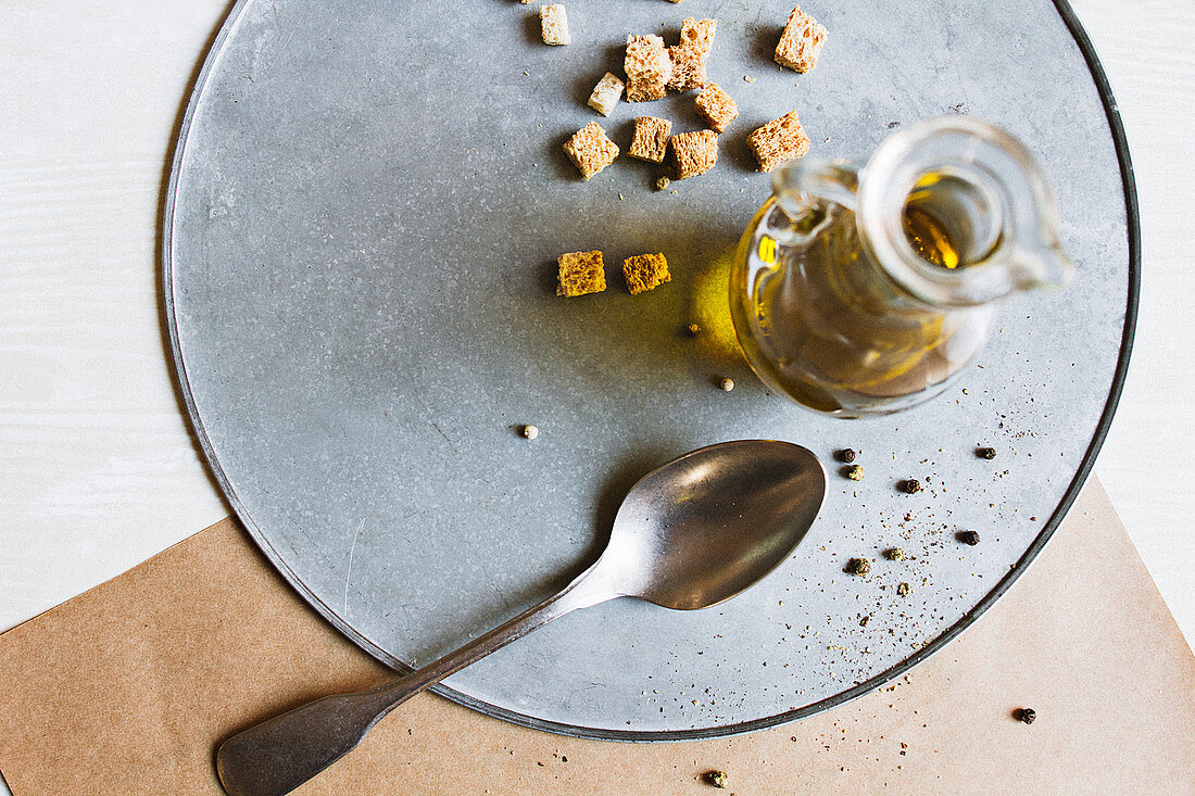 A small carafe of olive oil, croutons, a spoon and pepper on a plate
