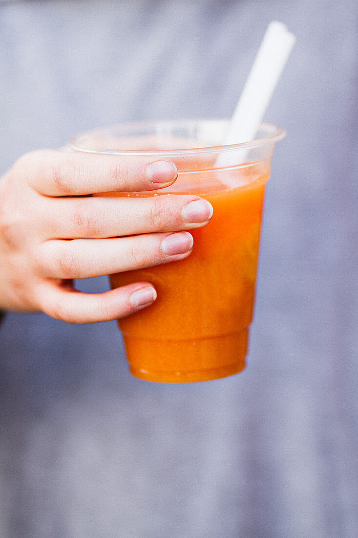 A hand holding a cup of fresh-pressed fruit juice