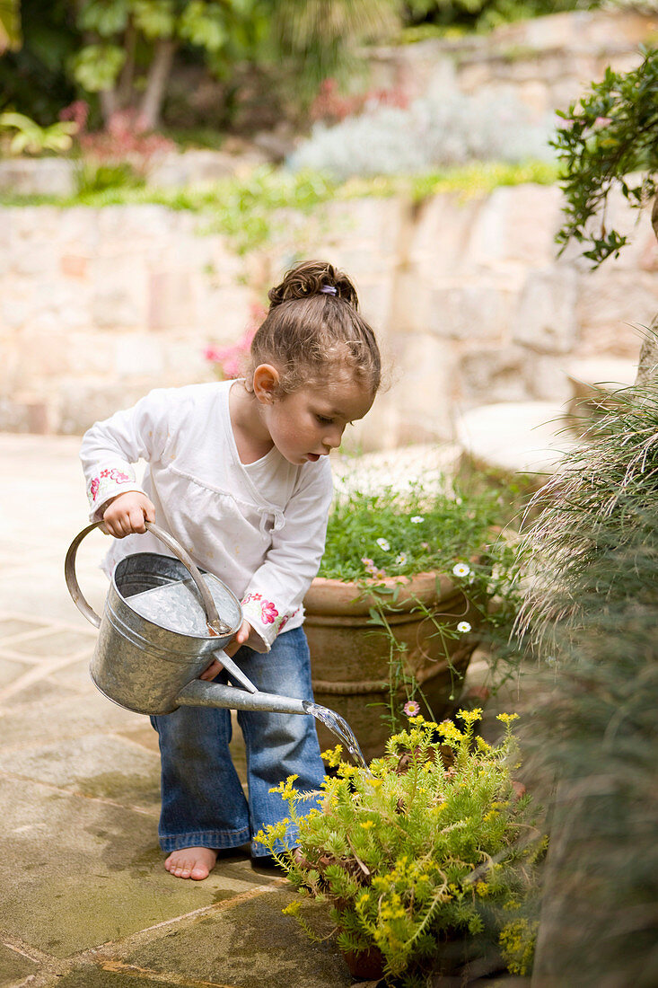 Little girl watering plants with watering can on stone terrace