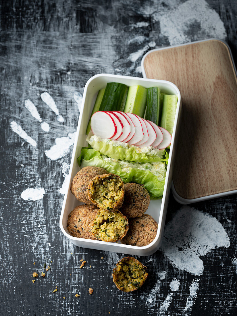 Falafel, a dip on lettuce leaves, radishes and cucumber in a lunchbox