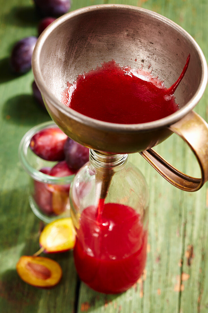 Homemade damson syrup being poured into a bottle using a funnel