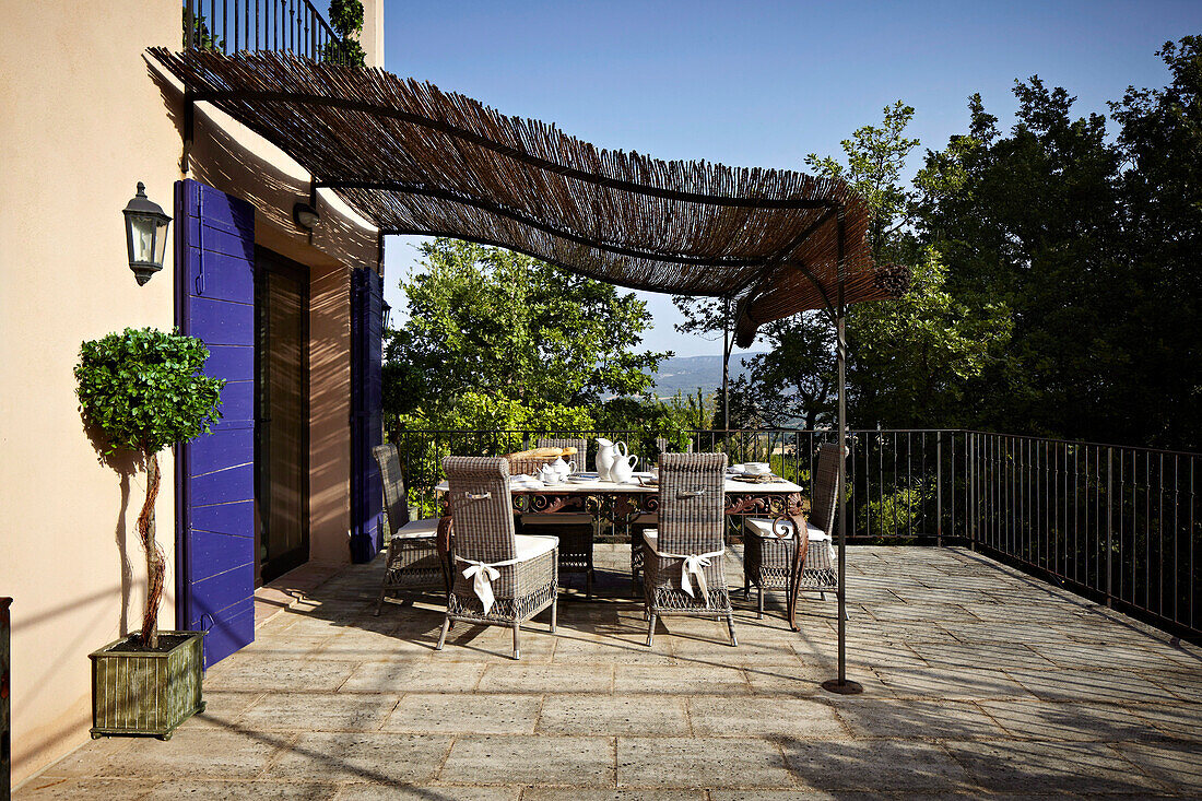 Marmortisch und Korbstühle auf strohüberdachter Terrasse eines französischen Landhauses