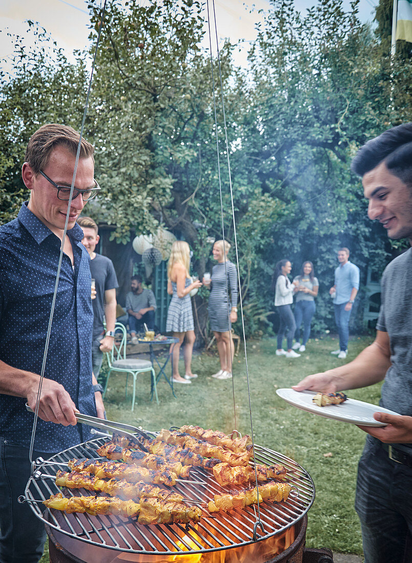 Men grilling turkey skewers on a hanging grill at a garden party